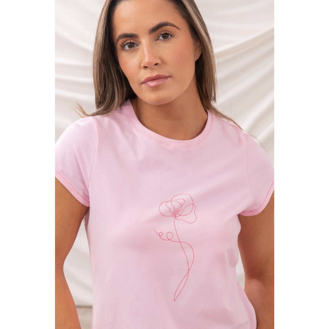 Woman wearing a pink Lighthouse short sleeve Causeway t-shirt with a single flower print on a white background