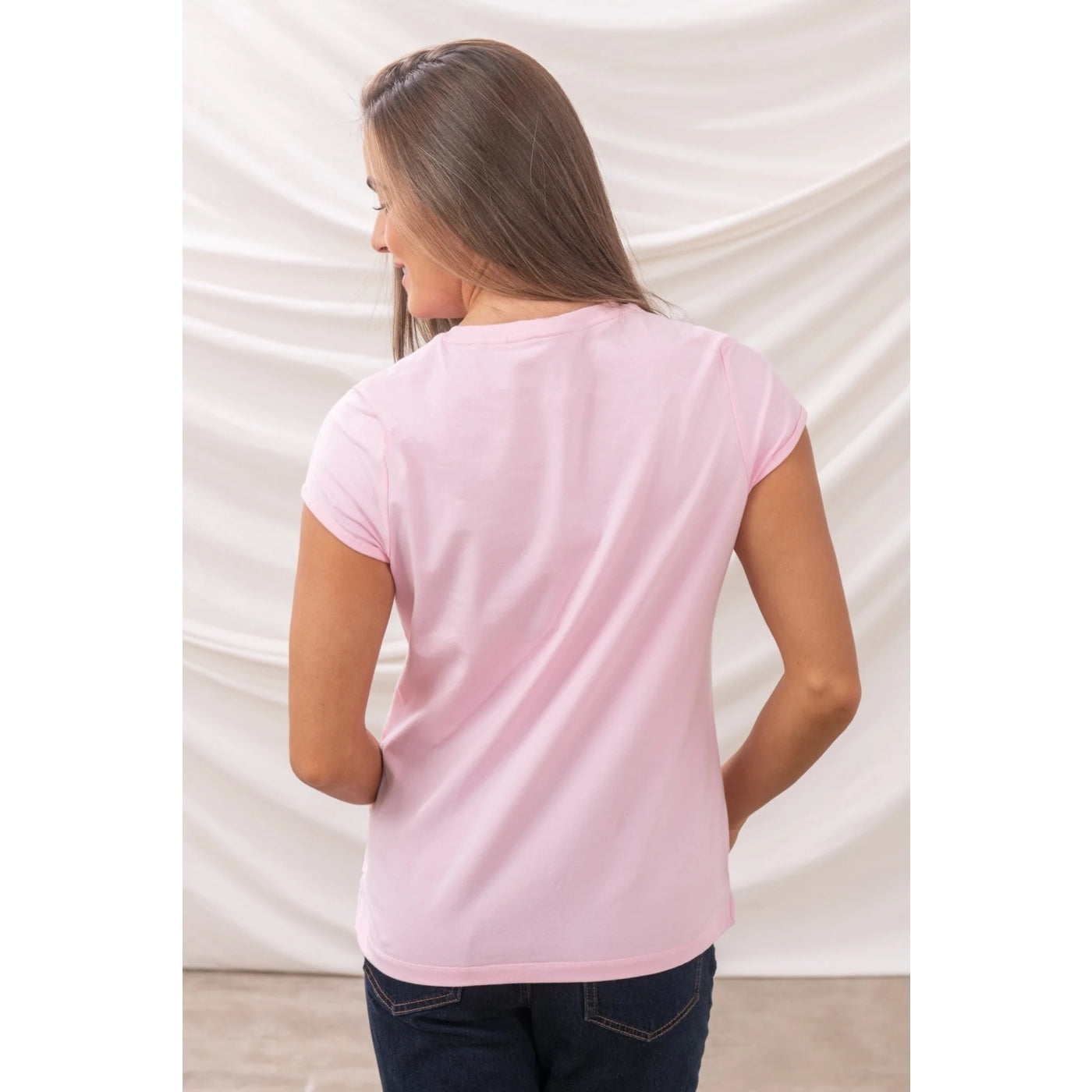 Back view of a woman wearing a light pink Lighthouse Causeway t-shirt against a white background