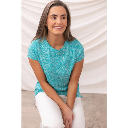 Woman wearing a Lighthouse short sleeve causeway t-shirt in Soft Teal with a floral pattern sitting on a white background