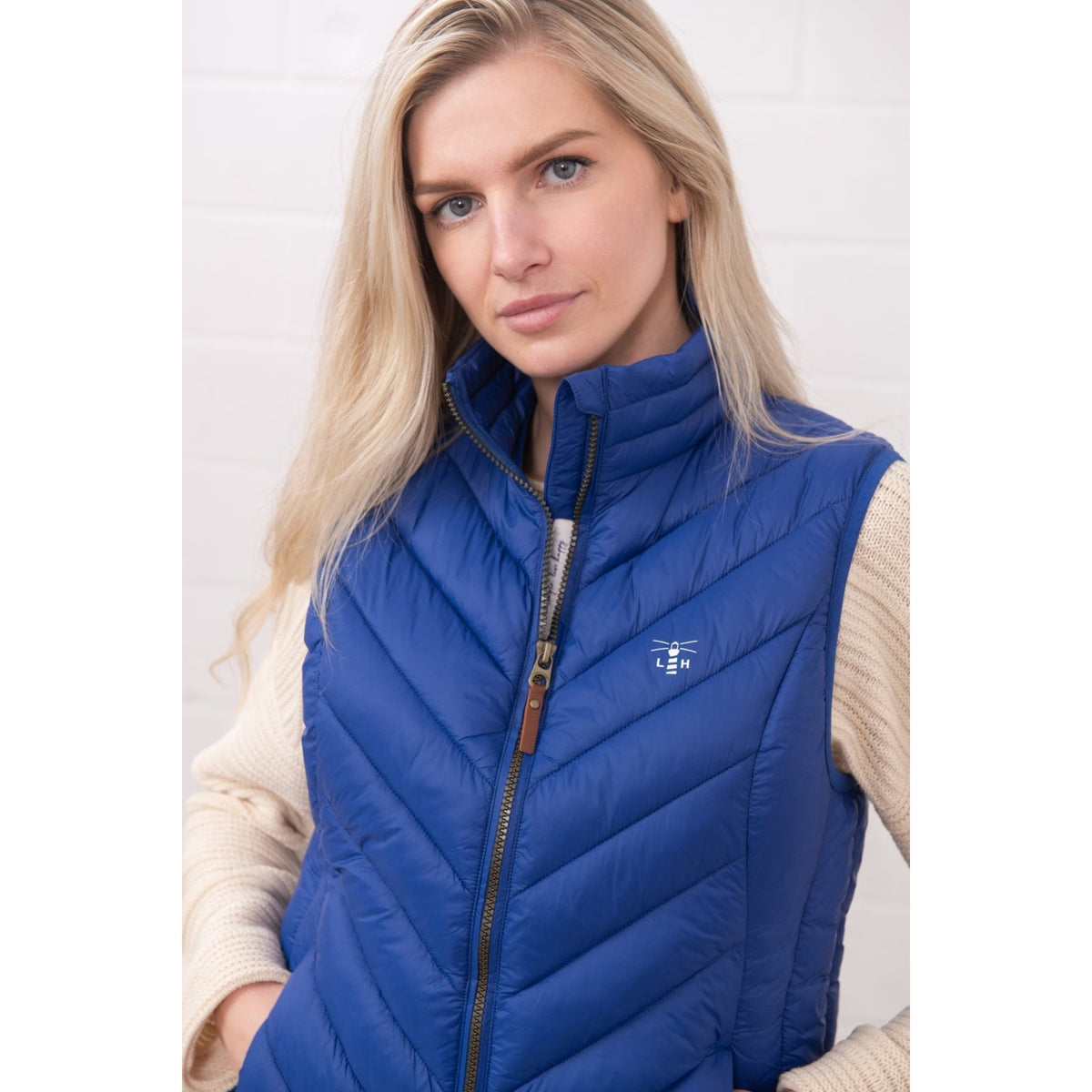 Close-up view of a woman wearing a Lighthouse padded Laurel Gilet in Indigo Blue over a cream jumper.