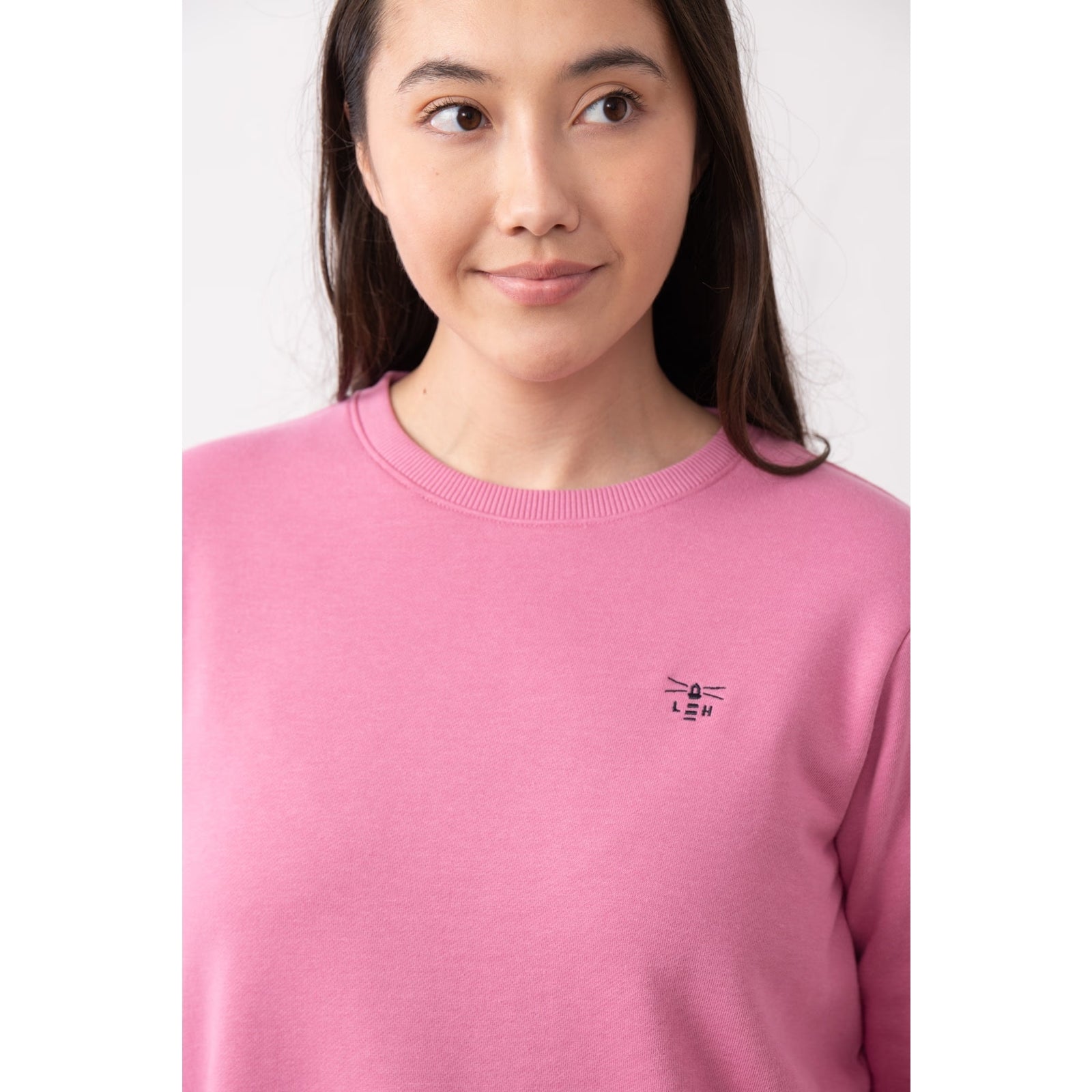 Close-up view of a woman wearing a Lighthouse Seaside crew neck sweatshirt in pink with small logo embroidered on one side of the chest and elasticated cuffs.