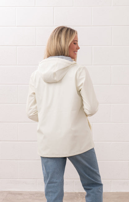 Back view of a woman wearing a white Lighthouse womens Coconut jacket with a hood and blue jeans