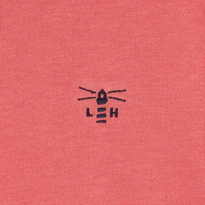 Close-up of a coral fabric with a black embroidered Lighthouse logo.