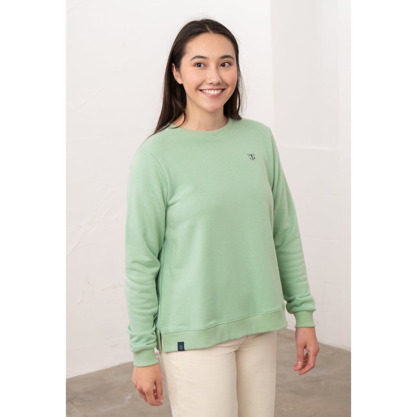 A woman wearing a Lighthouse Seaside crew neck sweatshirt in Pastel Green with small logo embroidered on one side of the chest and elasticated cuffs.