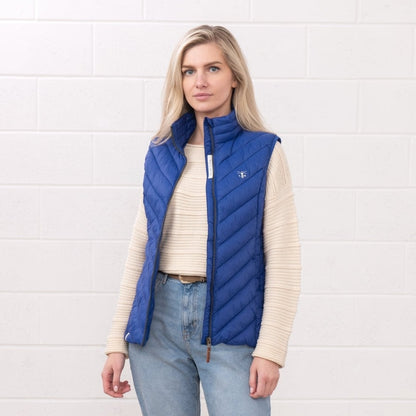 Front view of a woman wearing a Lighthouse padded Laurel Gilet in Indigo Blue unzipped over a cream jumper.