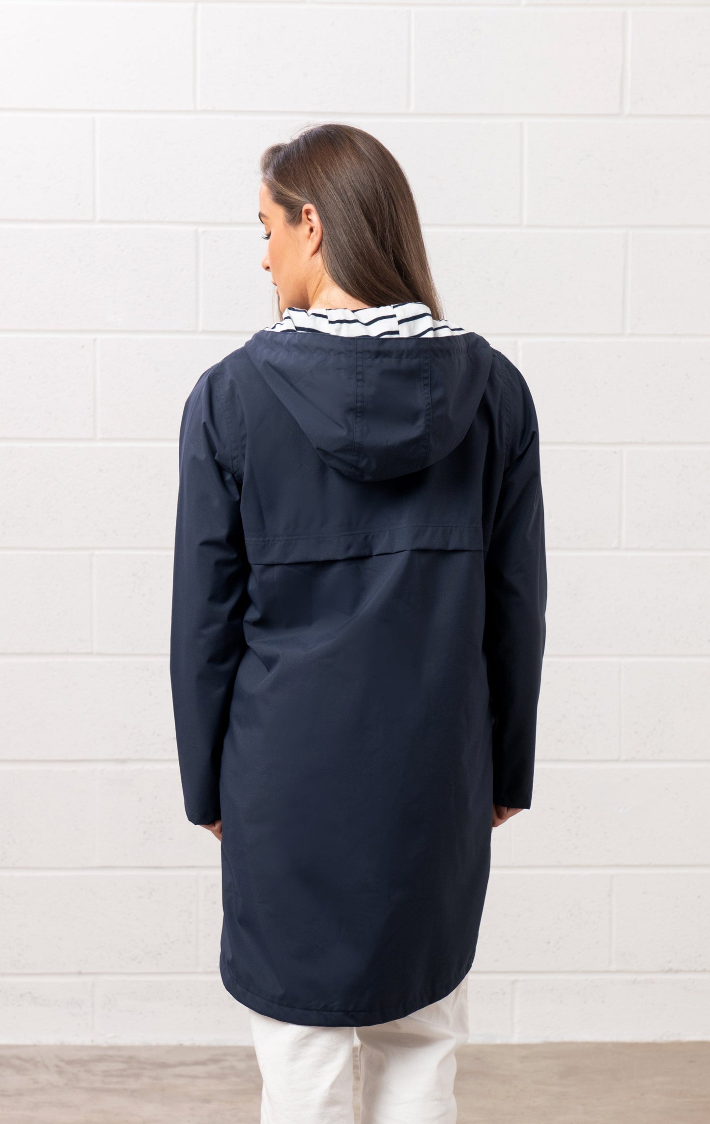 Back view of Lighthouse womens navy waterproof jacket with hood worn by female model indoors