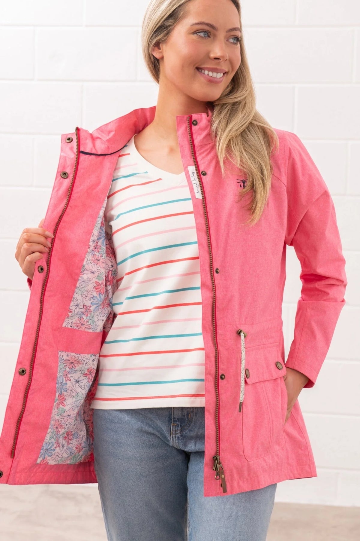 Lighthouse womens pink waterproof jacket open to show floral inner lining worn with striped shirt and jeans