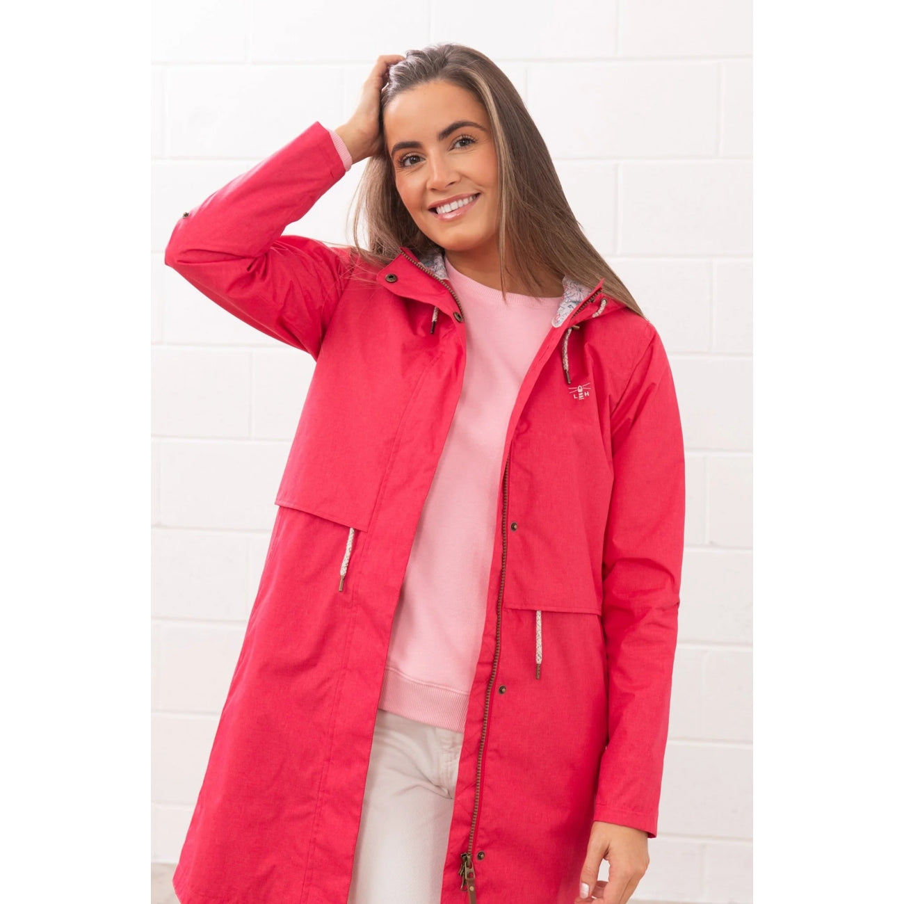 Woman wearing a Lighthouse Pippa 3/4 length waterproof raincoat in Raspberry pink/red.
