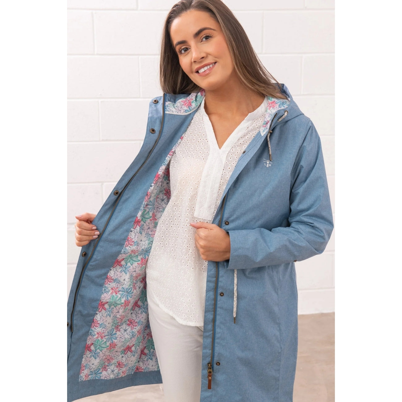 Woman wearing a Lighthouse Pippa 3/4 length waterproof raincoat in Soft Denim Blue, showing the multicoloured floral lining.