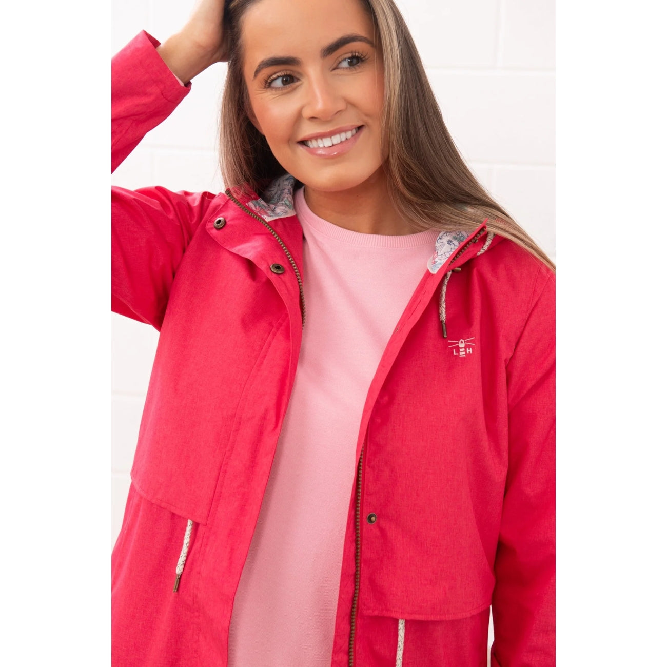 Close-up view of a woman wearing a Lighthouse Pippa 3/4 length waterproof raincoat in Raspberry pink/red.