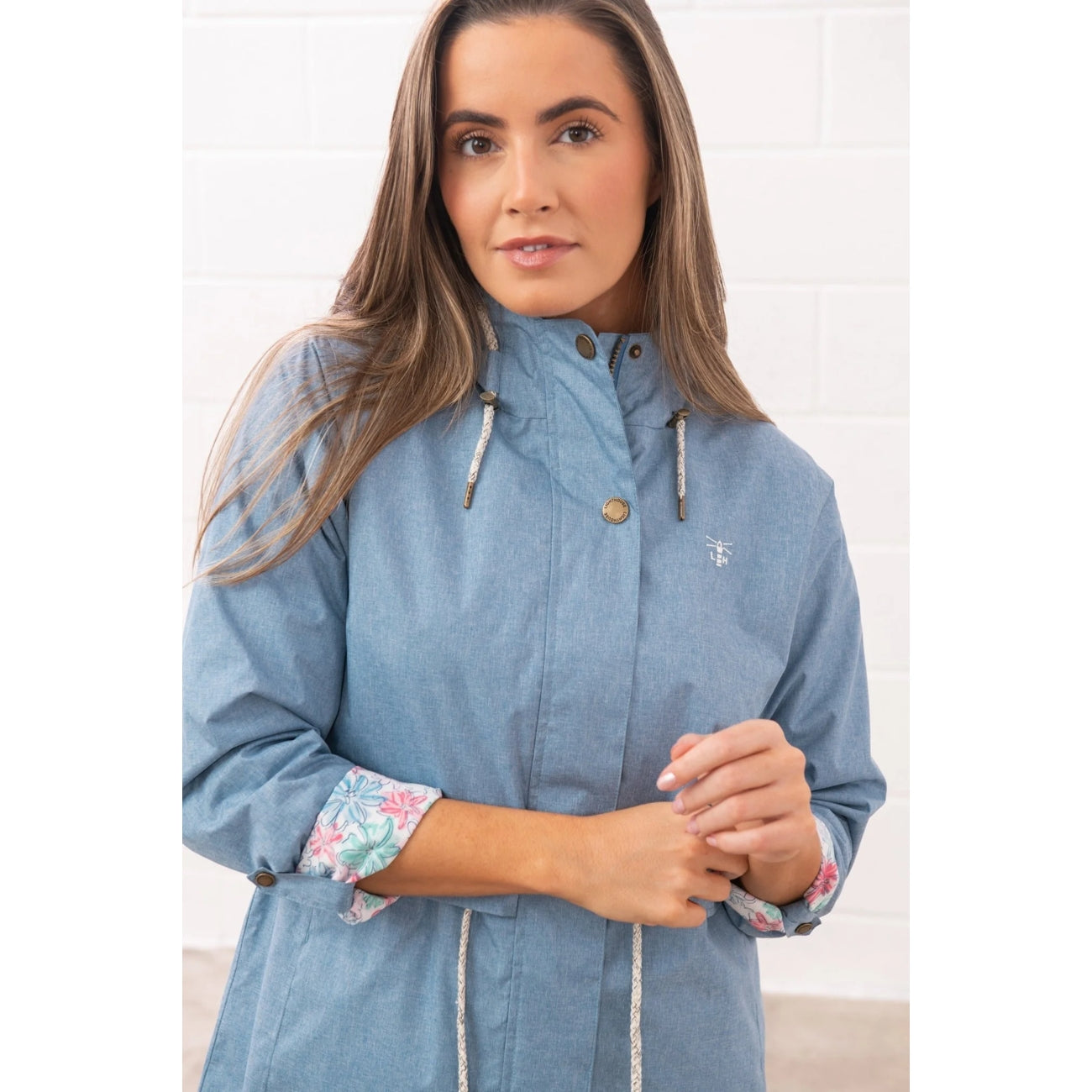 Woman wearing a Lighthouse Pippa 3/4 length waterproof raincoat in Soft Denim Blue with the sleeves turned up.