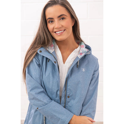 Close-up view of a woman wearing a Lighthouse Pippa 3/4 length waterproof raincoat in Soft Denim Blue with floral hood lining.