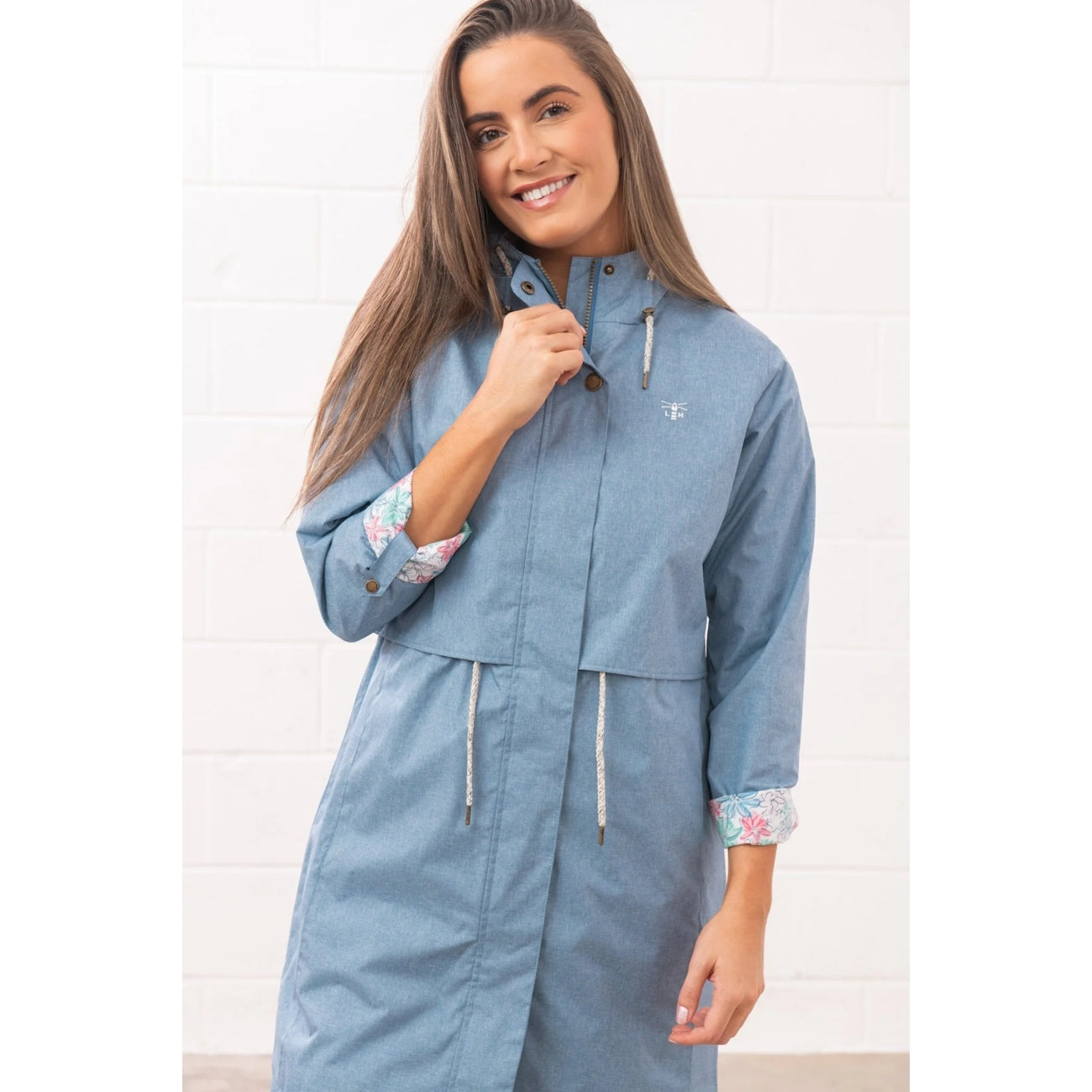 Front view of a woman wearing a Lighthouse waterproof Pippa 3/4 length raincoat in Soft Denim Blue with rolled back sleeves.