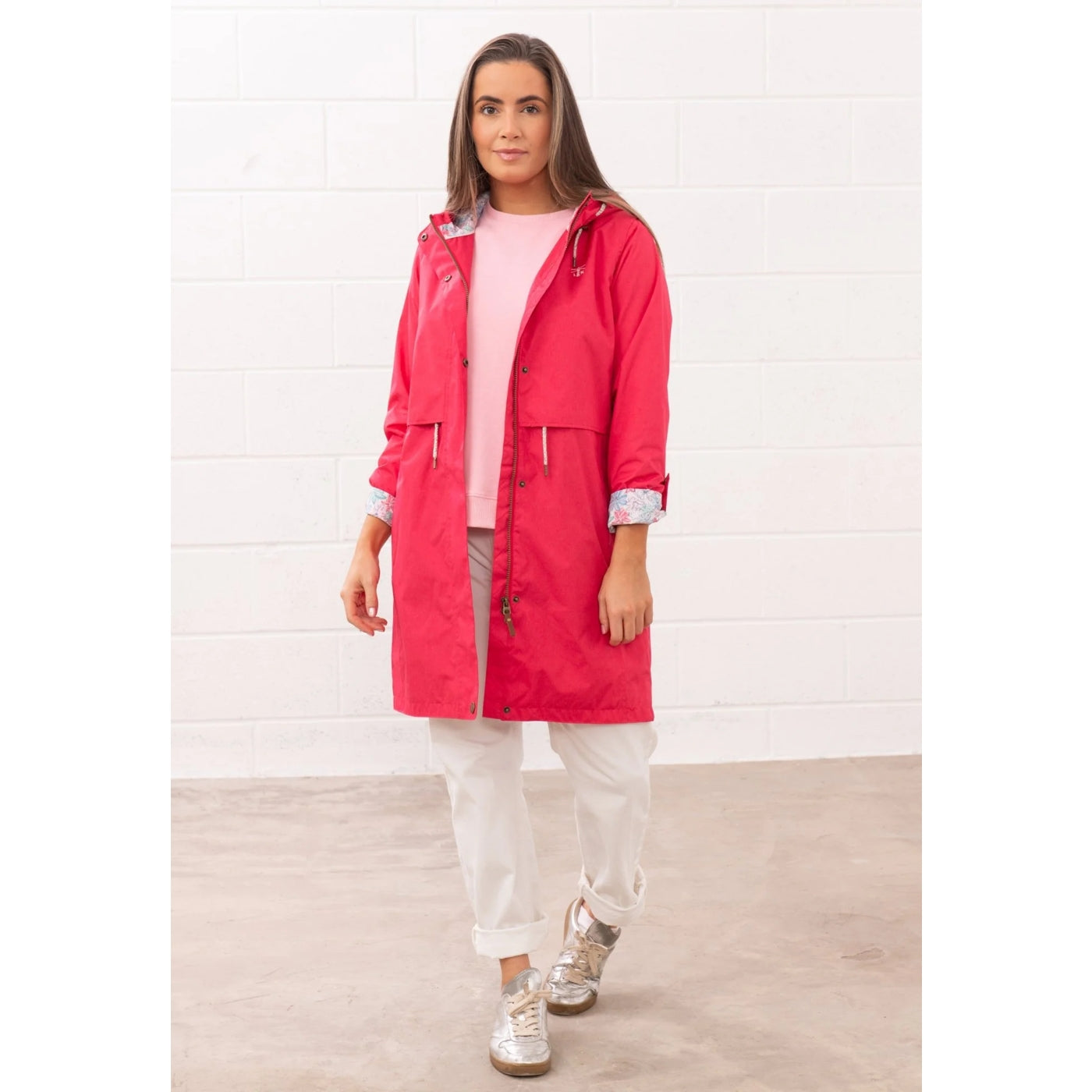 Woman wearing a Lighthouse Pippa 3/4 length waterproof raincoat in Raspberry pink/red with the sleeves turned up.