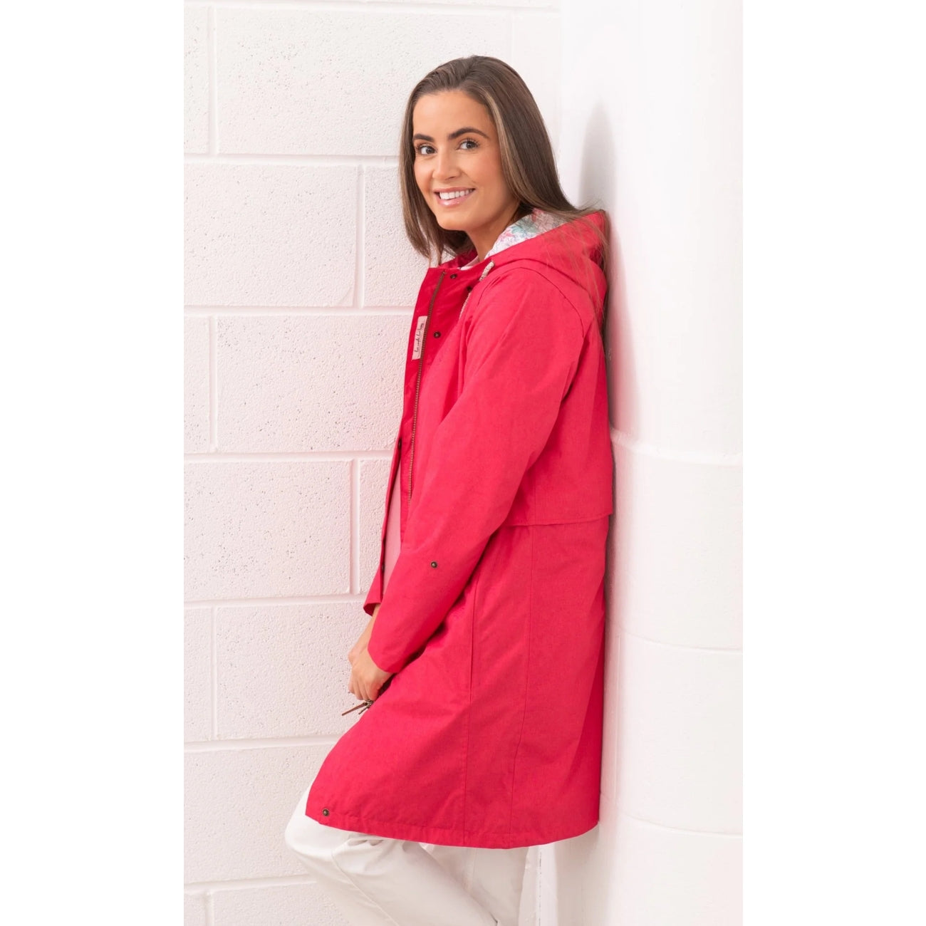 Side view of a woman wearing a Lighthouse Pippa 3/4 length waterproof raincoat in Raspberry pink/red.