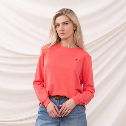 Woman wearing a Lighthouse coral Seaside sweatshirt with a small chest logo against a white background