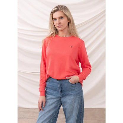 Woman wearing a coral Lighthouse sweatshirt and blue jeans against a plain background