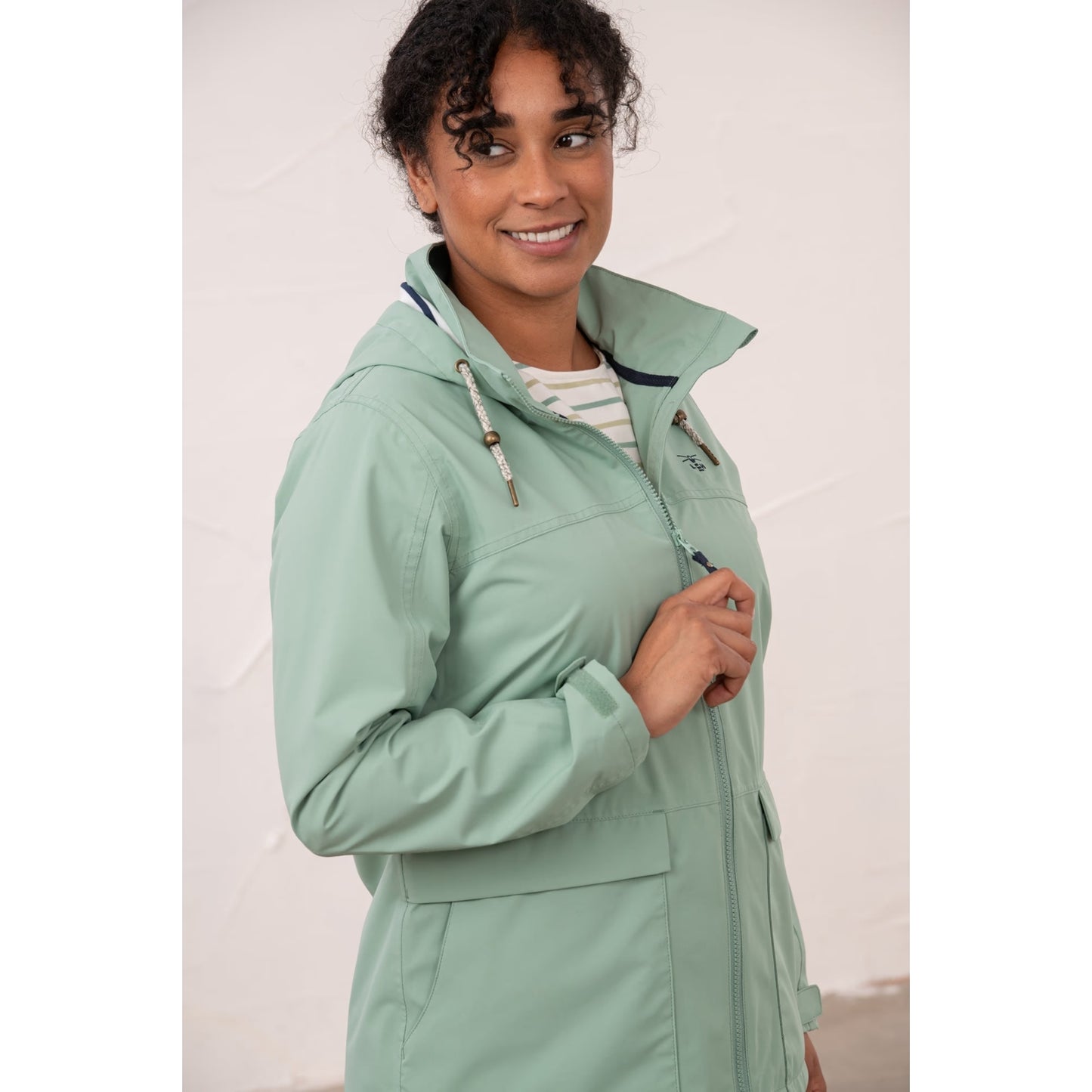 Close-up view of a woman wearing a Lighthouse waterproof Beachcomber II waterproof jacket in Basil green.