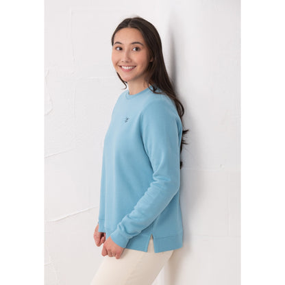 Side view of a woman wearing a Lighthouse Seaside crew neck sweatshirt in blue with small logo embroidered on one side of the chest, elasticated cuffs and side seam slits.
