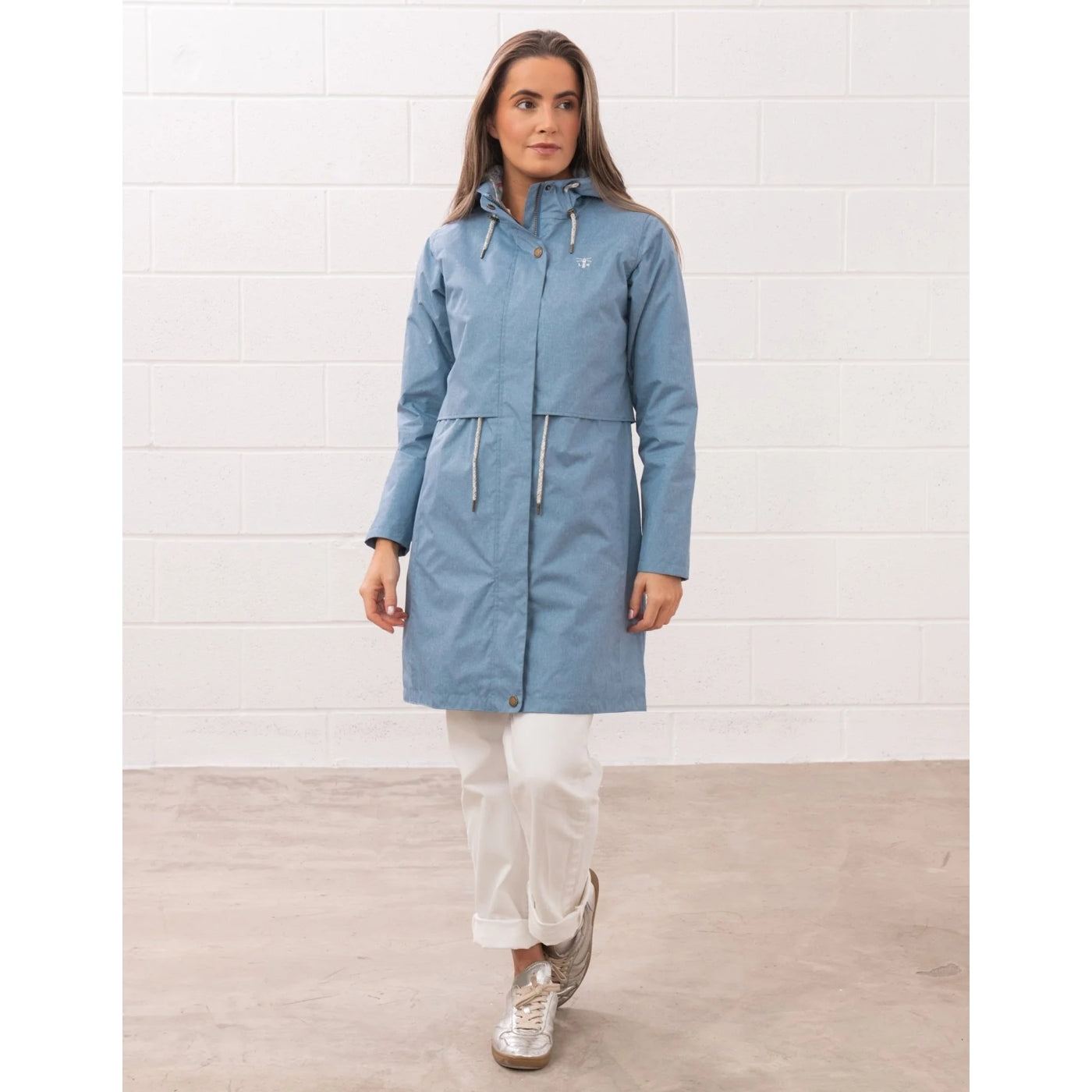 Woman wearing a Lighthouse Pippa 3/4 length waterproof raincoat in Soft Denim Blue zipped up.