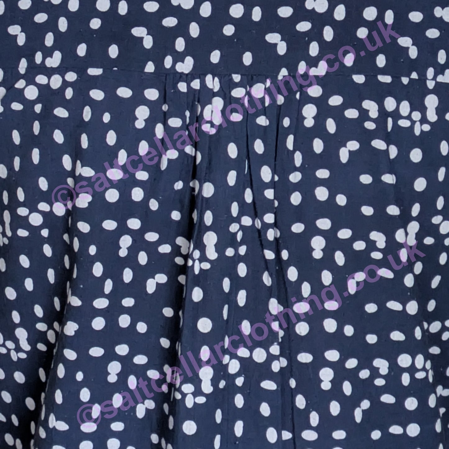 Close-up of navy fabric with a white dot pattern and pleats on a womens Mudd & Water Sunrise Blouse