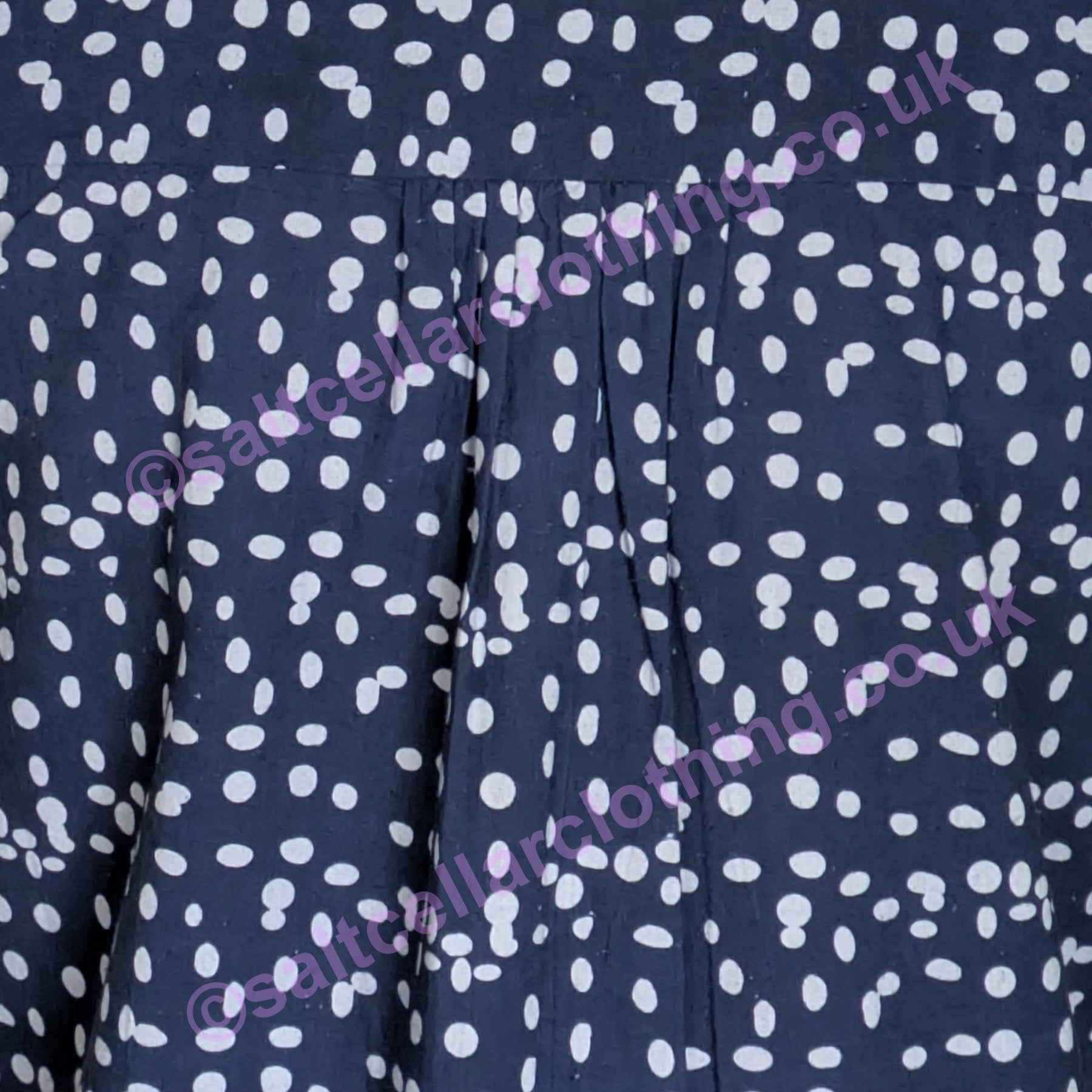 Close-up of navy fabric with a white dot pattern and pleats on a womens Mudd & Water Sunrise Blouse