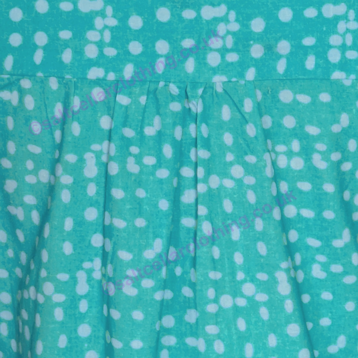 Close-up of a Mudd & Water Sunrise Blouse turquoise fabric with polka dot pattern and pleats