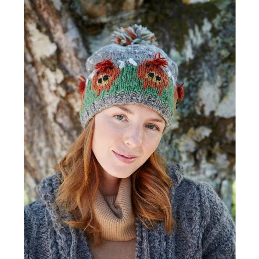 Woman wearing a knitted Pachamama hat with Highland Cow designs against a natural background