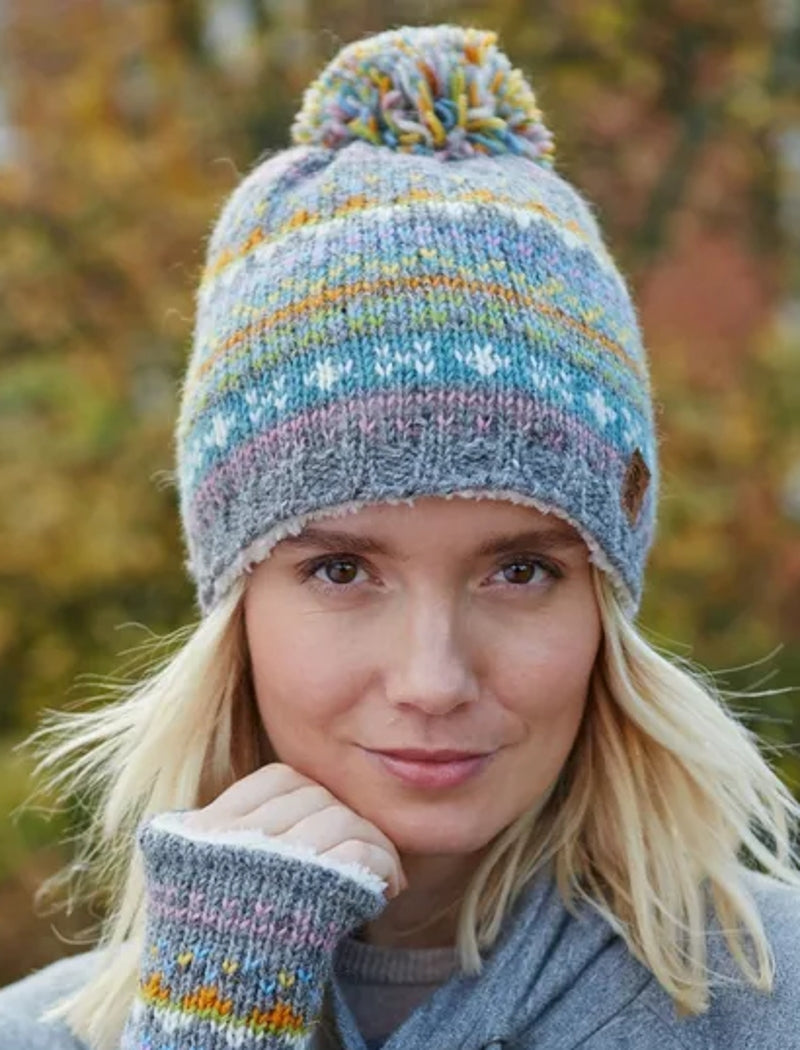 Woman wearing a Pachamama knitted Braemar bobble hat beanie in grey and multicolour Fair Isle pattern.