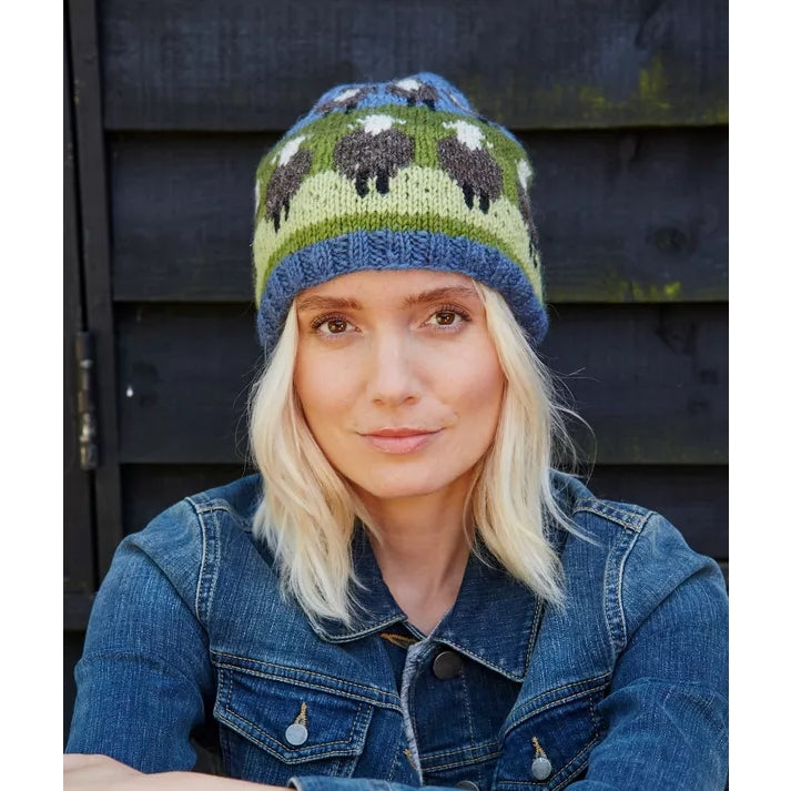 Woman wearing a knitted Pachamama hat with sheep pattern against a dark wooden background