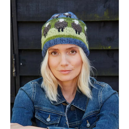 Woman wearing a knitted Pachamama hat with sheep pattern against a dark wooden background