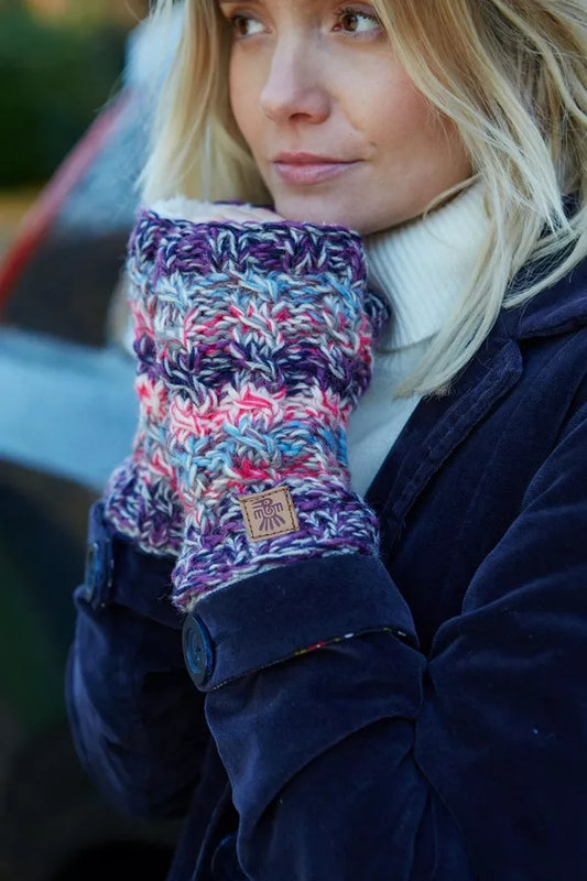 A woman wearing pink and purple knitted Pachamama Utrecht handwarmers with a multicolour stripe pattern.