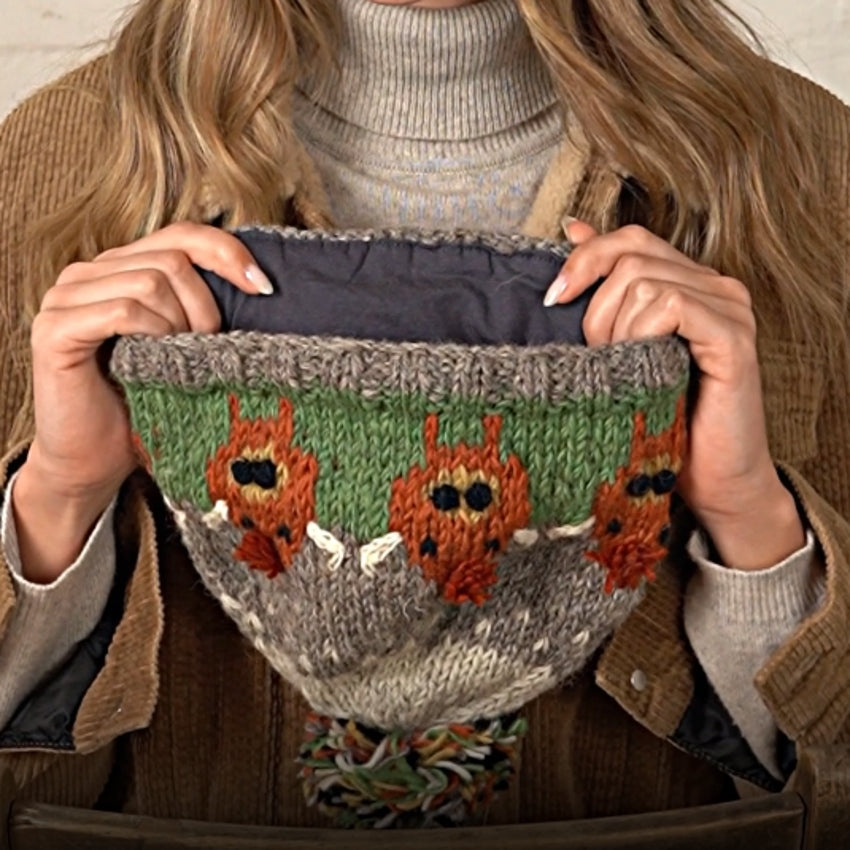 Woman holding a knitted Pachamama Highland Cow pattern hat with a jersey cotton lining.