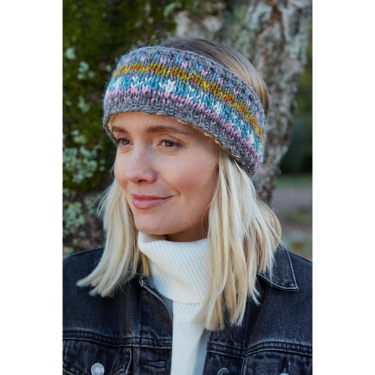 Front view of a woman wearing a colourful knitted Pachamama Braemar headband with an outdoor background