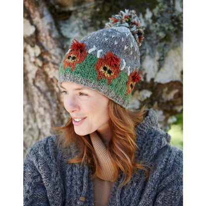 Main view of a woman wearing a Pachamama knitted bobble hat with a Highland Cow design against a natural background