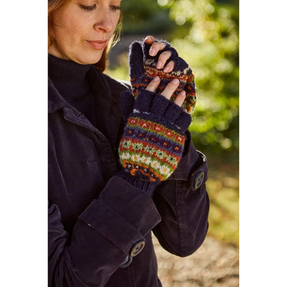 Person wearing a dark coat and colourful Pachamama knitted mittens outdoors.