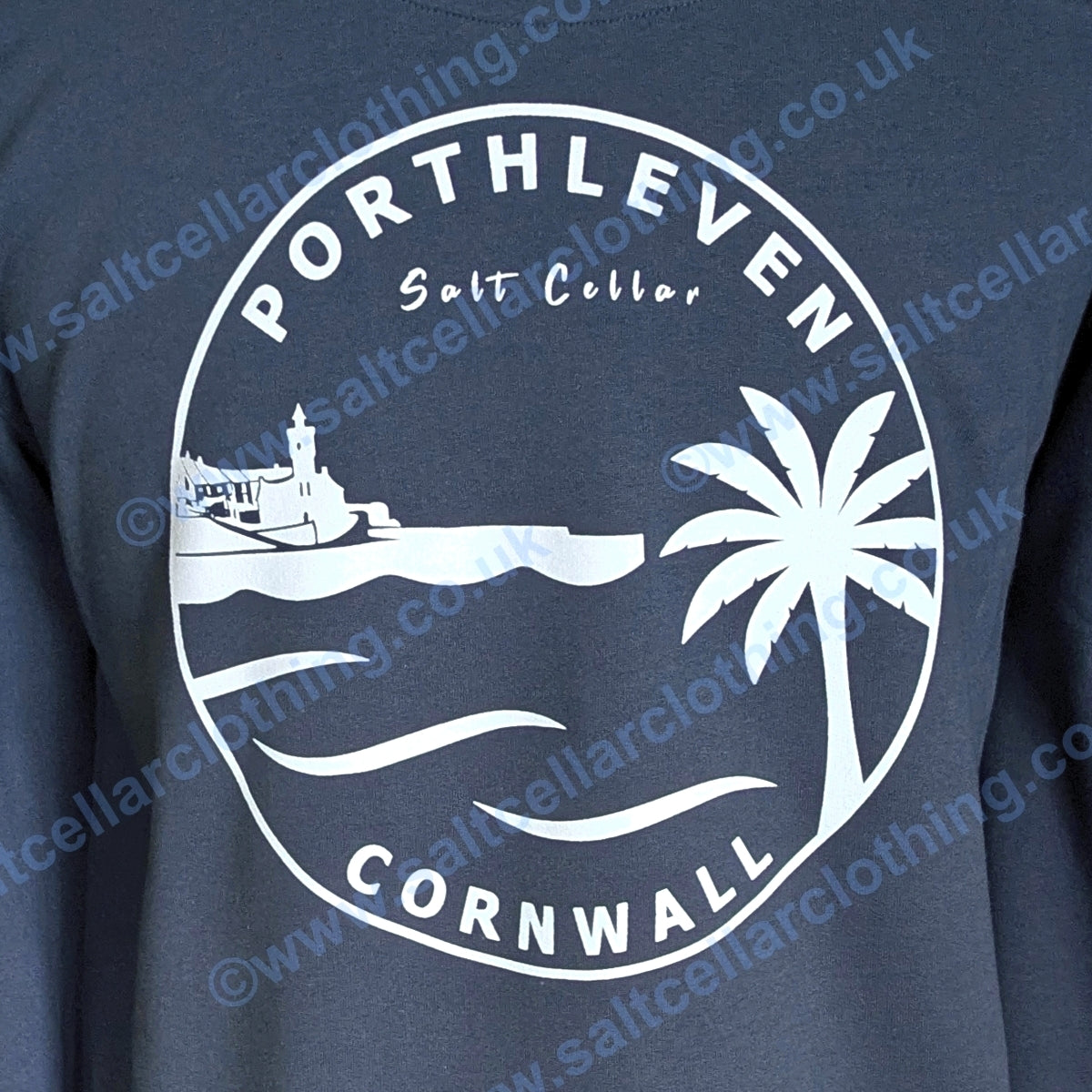 A close-up view of a Petrol blue unisex crewneck sweatshirt, featuring a large white circular graphic print that reads 'PORTHLEVEN Salt Cellar CORNWALL' with a harbourside clocktower, palm tree, and waves.