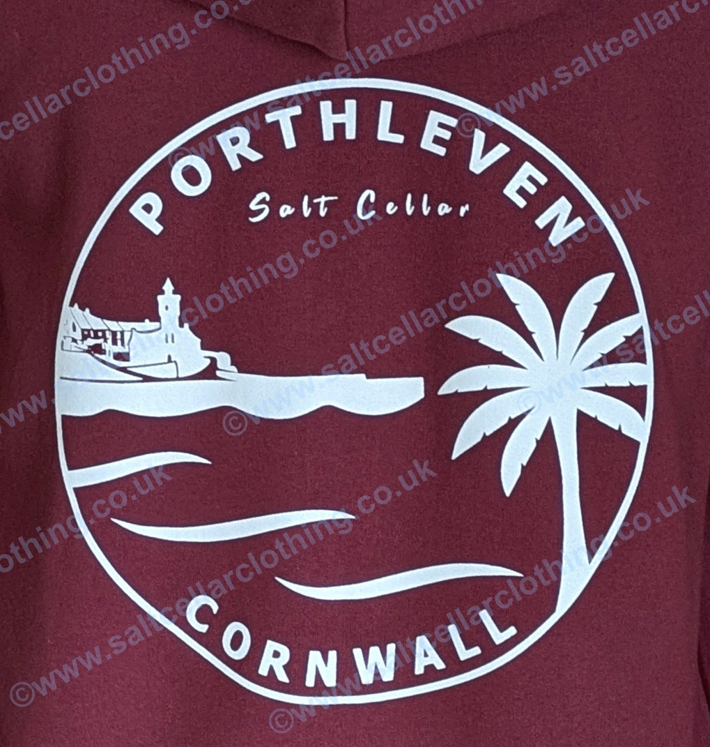 Close-up view of the print on a Burgundy Red full zip hoodie, featuring a white circular graphic, with a clocktower and harbour, palm tree, waves, and the text 'PORTHLEVEN Salt Cellar' and 'CORNWALL'.