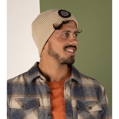 Man wearing a Saltrock light brown SR beanie and plaid shirt against a green and white background