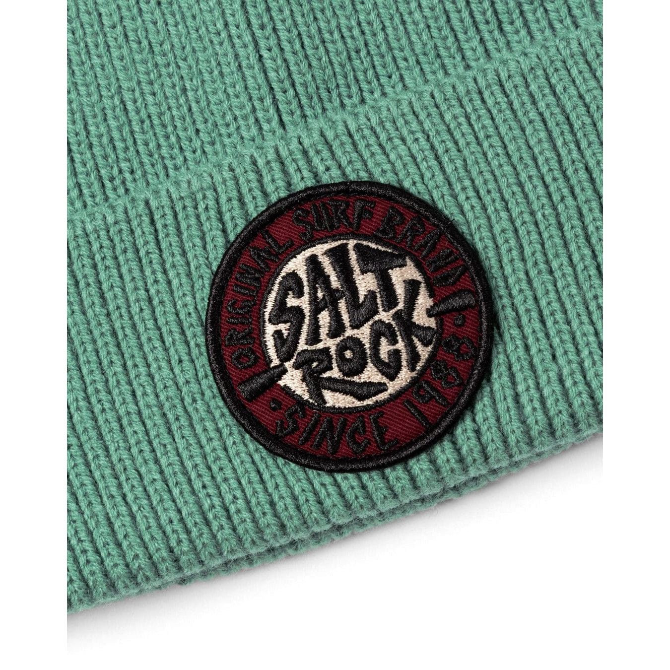 Close-up of a turquoise green knitted beanie with a turn-up hem and round 'Salt Rock' logo on a white background
