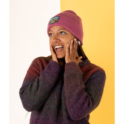 Woman wearing a Saltrock Uplands  dark pink knitted beanie and sweater against a yellow background