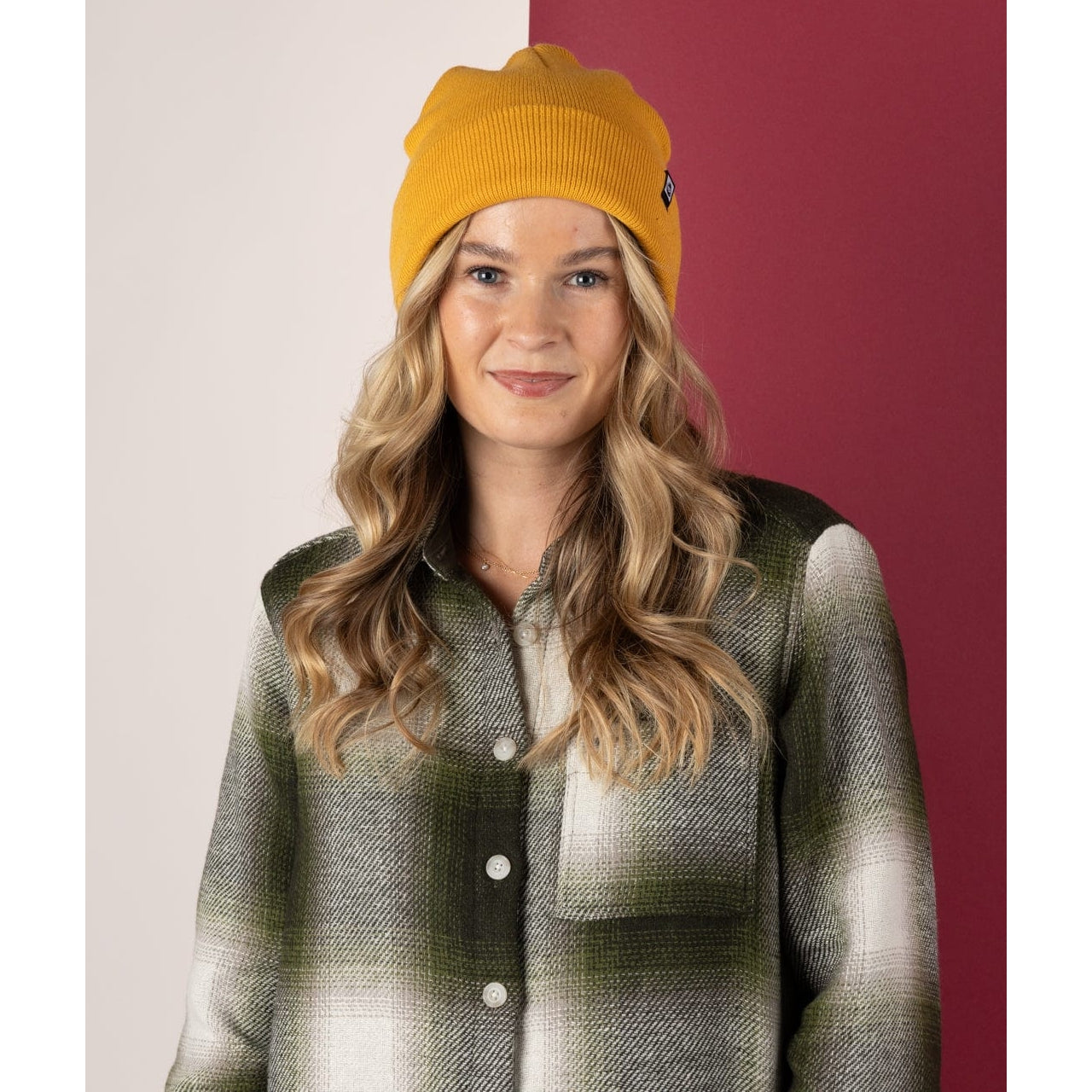 Woman wearing a Saltrock yellow Ok beanie and plaid shirt against a two-tone background