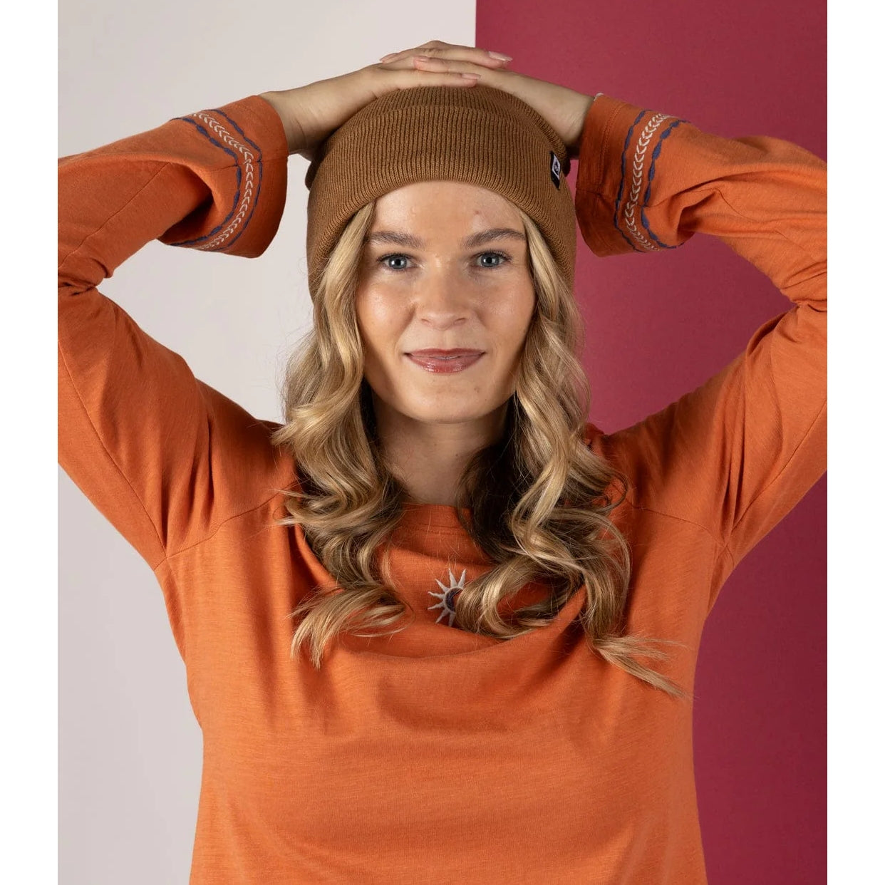 Woman wearing an orange sweater and brown Saltrock beanie against a two-tone background