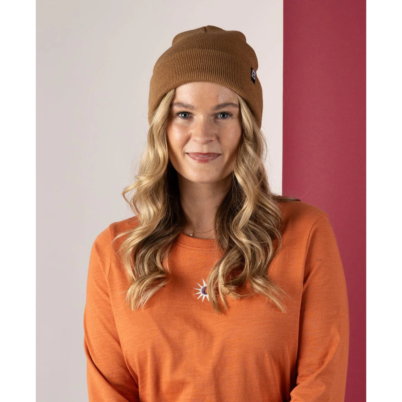 Woman wearing a brown Saltrock OK beanie and orange shirt with a logo against a white and red background