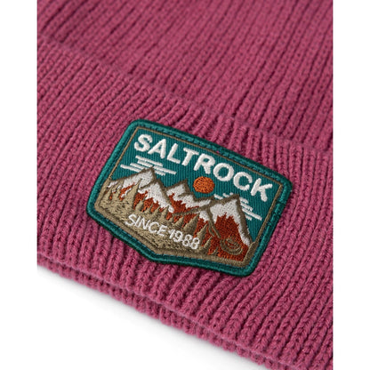 Close up of a dark pink knitted beanie with turn-up hem and Saltrock mountains logo patch on a white background