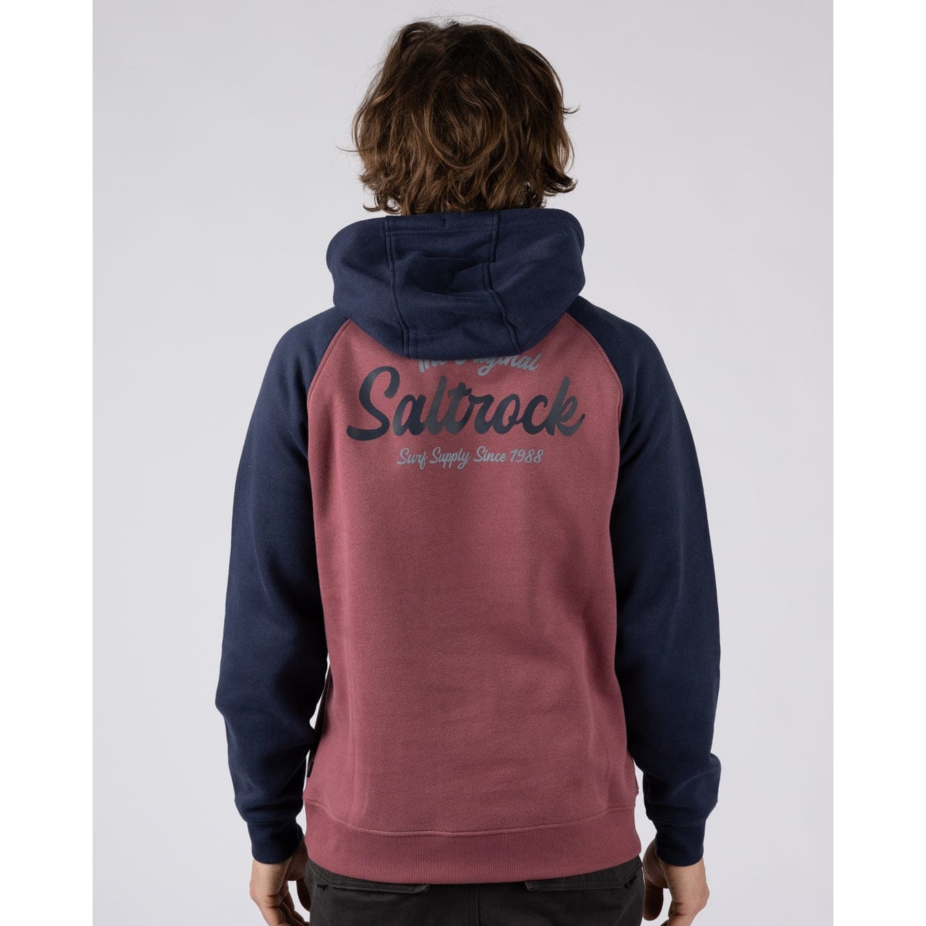 Back view of a man wearing a Saltrock Postcard Script hoodie in dark pink with navy blue sleeves and hood and large logo print