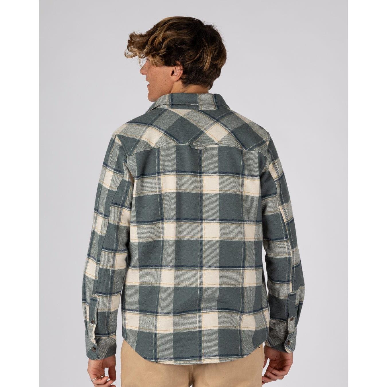 Back view of a man wearing a Saltrock Strait long sleeve check shirt in dark teal green with chest pockets and tan trousers