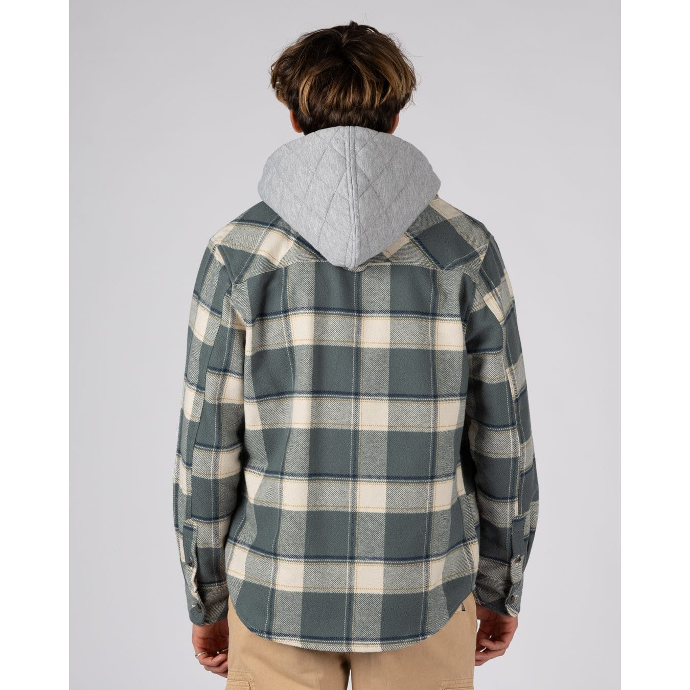 Back view of a man wearing a mens Saltrock Strait long sleeve check shirt in dark teal green with chest pockets and a detachable grey hood with tan trousers