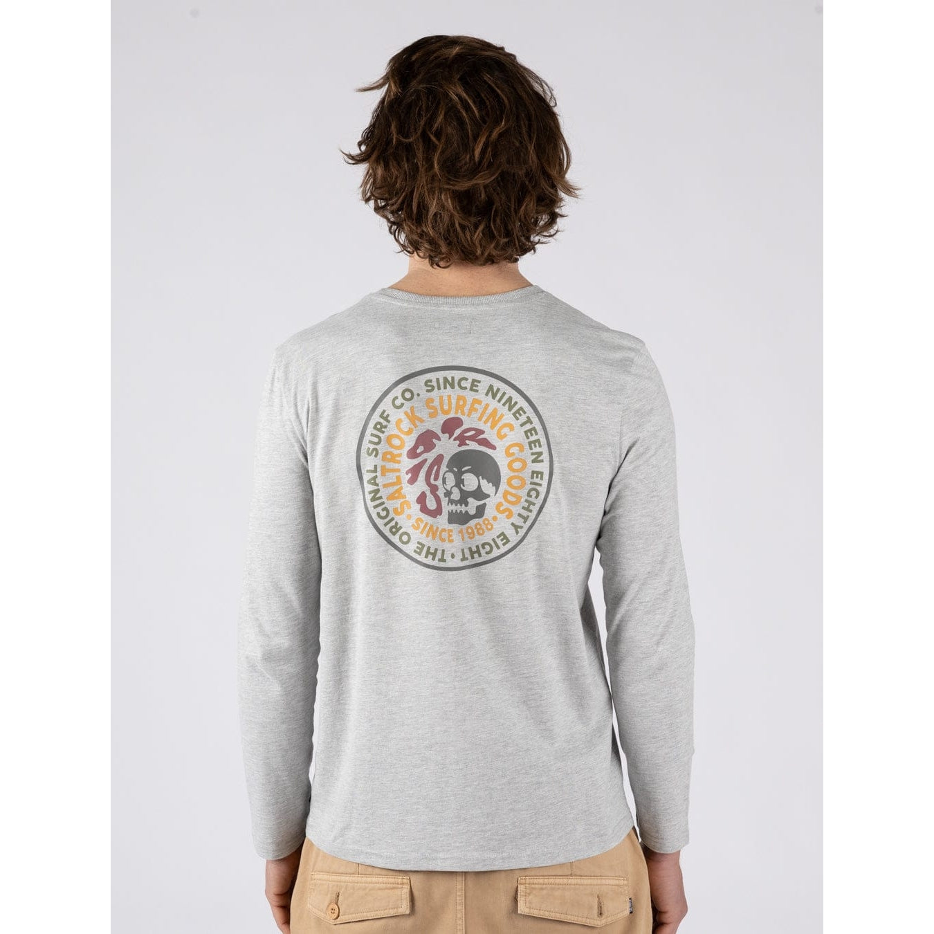 Back view of a man wearing a Saltrock Trail Badge long sleeve t-shirt in grey with a circular surf and skull themed print