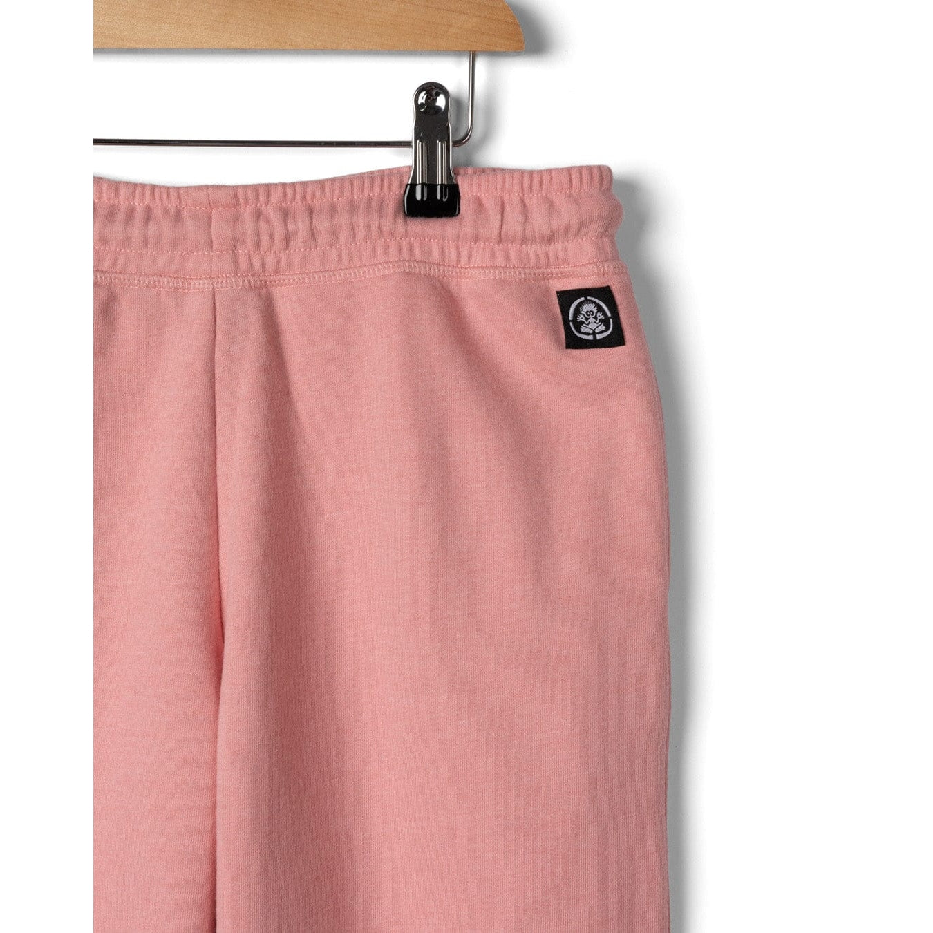 Close-up view of a small black logo label on the back of a pair of Saltrock kids Norie jogger trousers in pink